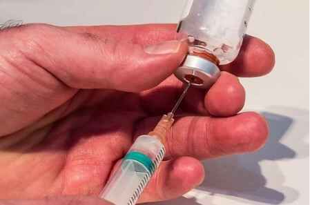Uma pessoa retirando a penicilina de um frasco com uma injeção.